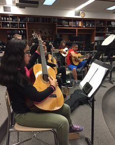 a group of people playing guitars in a room filled with books and music equipment,