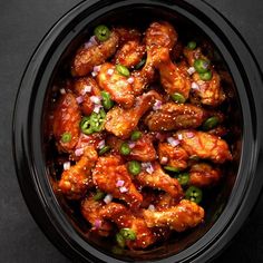 chicken wings with onions and green peppers in a slow cooker on a black surface