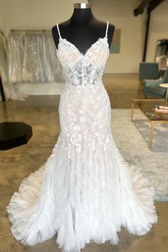 a white wedding dress on display in a room with chairs and other items behind the mannequin