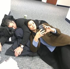 two people laying on the floor looking at their cell phones