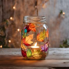 a glass jar filled with colorful leaves on top of a wooden table next to christmas lights