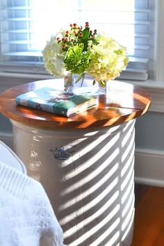 a vase with flowers sitting on top of a wooden table next to a white bed