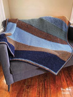 a blue and brown blanket sitting on top of a couch next to a wooden floor