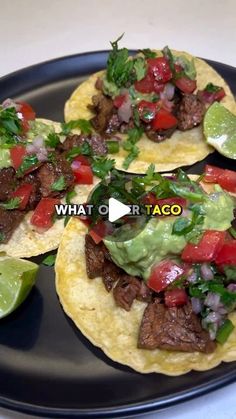 three tacos on a black plate with avocado and tomatoes