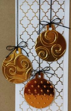 three gold and silver ornaments hanging on a white board with black string attached to it