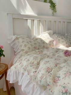 a white bed topped with lots of pillows next to a wooden table filled with flowers