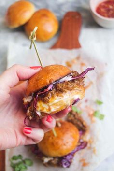 a hand holding a sandwich with meat and onions on it, in front of other food items