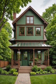 a green house with brown trim on the front and side windows, surrounded by greenery