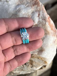 a person's hand holding a turquoise and white ring with a diamond in it