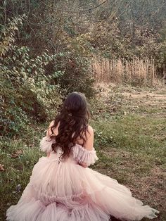 a woman in a pink dress sitting on the ground next to some bushes and trees