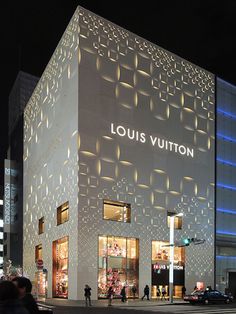 people are walking in front of the louis vuitton department store at night time