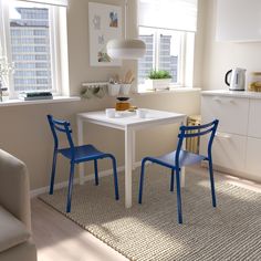 two blue chairs sitting at a white table in a living room next to a window