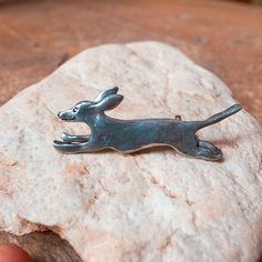 a metal dog brooch sitting on top of a rock