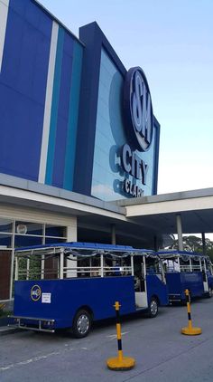 three blue buses parked in front of a building with a sign that says om city