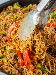 someone using a fork to stir noodles in a skillet with broccoli and peppers