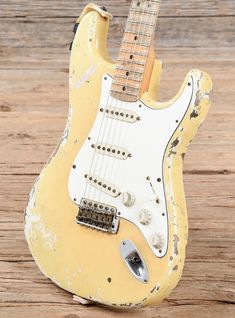 an old yellow guitar sitting on top of a wooden floor