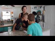 a woman and two boys are in the kitchen with one boy looking at something on the counter