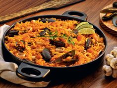 a pan filled with rice and mussels on top of a wooden table