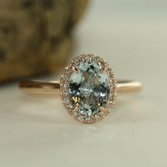 an oval cut aquamarinee and diamond ring on a white surface with a rock in the background