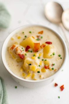 a white bowl filled with potato soup next to two spoons and an egg on the side