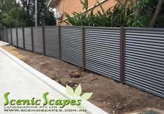 a fence that is next to a building with plants growing out of the ground in front of it