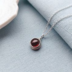 Garnet Necklace, Sterling Silver Necklace, Dainty Necklace, January Birthstone, Birthstone Jewelry DESCRIPTION This minimalist sterling silver necklace features a deep red Garnet cabochon.  The necklace would make a lovely birthday gift for a loved one, close friend or family. Garnet is a birthstone for January. The necklace comes in a lovely fabric pouch as standard. If you would prefer for your jewellery to be presented in a pretty gift box instead, please add it to your order using the drop down menu above.   FEATURES Gemstone: 8mm Natural Garnet Cabochon  Pendant height: 1.5 cm Pendant width: 1 cm Chain: .925 sterling silver chain with soldered links for extra strength Please note that this is a handmade item, so no two are ever exactly alike. Your necklace may look slightly different Red Birthstone Necklace, Garnet Birthstone Necklace For Jewelry Making, Garnet Birthstone Necklaces For Jewelry Making, Red Birthstone Necklace With Round Stone, Garnet Birthstone Round Necklace, Red Gemstone Birthstone Necklace In Sterling Silver, Red Sterling Silver Necklace With Round Pendant, Dainty Garnet Necklace For Gift, Silver Garnet Birthstone Necklace