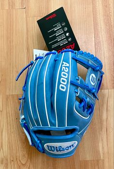 a blue baseball glove sitting on top of a wooden floor next to a black book