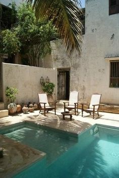 an empty pool with chairs around it in front of a white stucco building and palm trees