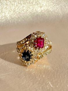 Antique 18k yellow gold ring featuring 36 old cut diamonds surrounding a crossover of sapphire and ruby central stones. Great antique condition Size: 6.25 resizable** Weight: 4.6 grams Band: 16.0 mm (front), 3.3 mm (back) Ruby: 5.0 mm x oval cut  Sapphire: 5.0 mm x oval cut Diamonds: 2.0 mm x 36 old cuts Please note, vintage and antique jewelry may come with imperfections commensurate of their age. To see more photos and videos of this piece, visit our Instagram: www.instagram.com/23carat Vintage Multi-stone Ruby Ring, Gold Victorian Ruby Ring With Single Cut Diamonds, Victorian Yellow Gold Ruby Ring With Single Cut Diamonds, Vintage Multi-stone Ruby Cluster Ring, Vintage Ruby Multi-stone Cluster Ring, Vintage Ruby Cluster Ring With Multi-stones, Gold Ruby Ring With Rose Cut Diamonds Cluster, Yellow Gold Sapphire Ring With Rose Cut Diamonds Cluster, Gold Sapphire Ring With Rose Cut Diamonds Cluster