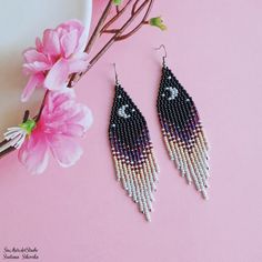 two pairs of beaded earrings sitting on top of a pink table next to flowers