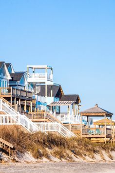 several beach houses on the sand with steps leading up to them