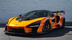 an orange and black sports car parked in front of a wall