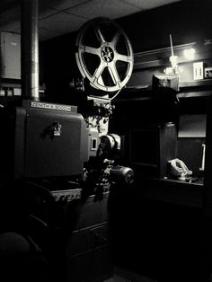 a black and white photo of an old movie projector in a dark room with other equipment