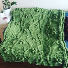 a green crocheted blanket sitting on top of a wooden table next to a potted plant