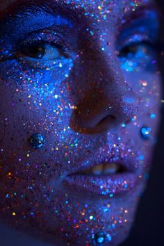 a woman's face is covered in blue and multicolored glitter as she stares at the camera