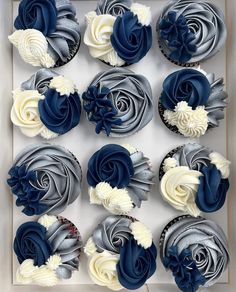 twelve cupcakes in a box decorated with blue and white frosting, roses and leaves