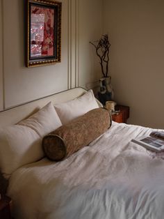 a bed with white linens and pillows in a bedroom next to a painting on the wall