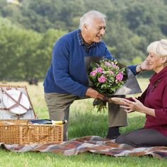 an older man giving flowers to a woman on the grass