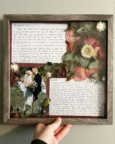 a person holding up a framed photo with flowers and leaves in the frame on top of it