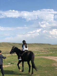 a woman riding on the back of a black horse next to a boy in a field