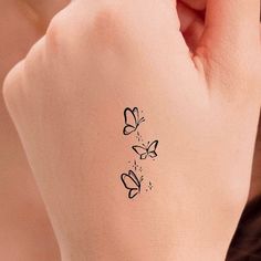 a woman's hand with a small tattoo on the wrist and two butterflies flying around