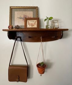 a wooden shelf with two hanging plants and a purse on the wall next to it