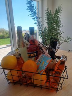 a basket filled with liquor and oranges on top of a wooden table next to a window