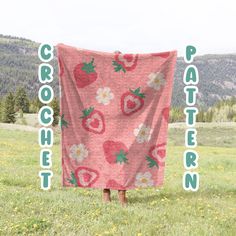 a pink blanket with strawberries and daisies on it in the middle of a field