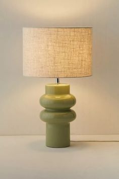 a green table lamp with a beige shade on it and a white wall in the background