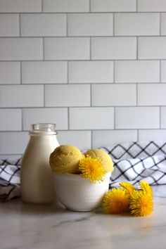 some yellow flowers in a white bowl next to a milk bottle on a marble counter