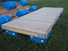 a large wooden trailer with blue barrels on it's side in the middle of some grass