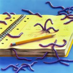 an open notebook with purple worms crawling around it and a pencil on top of the book