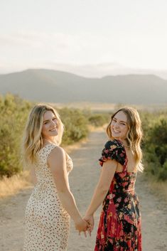 two women holding hands walking down a dirt road