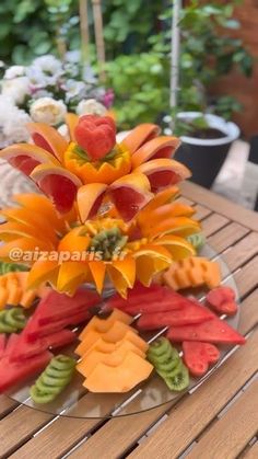 an arrangement of fruits and vegetables on a glass plate sitting on a wooden table outside